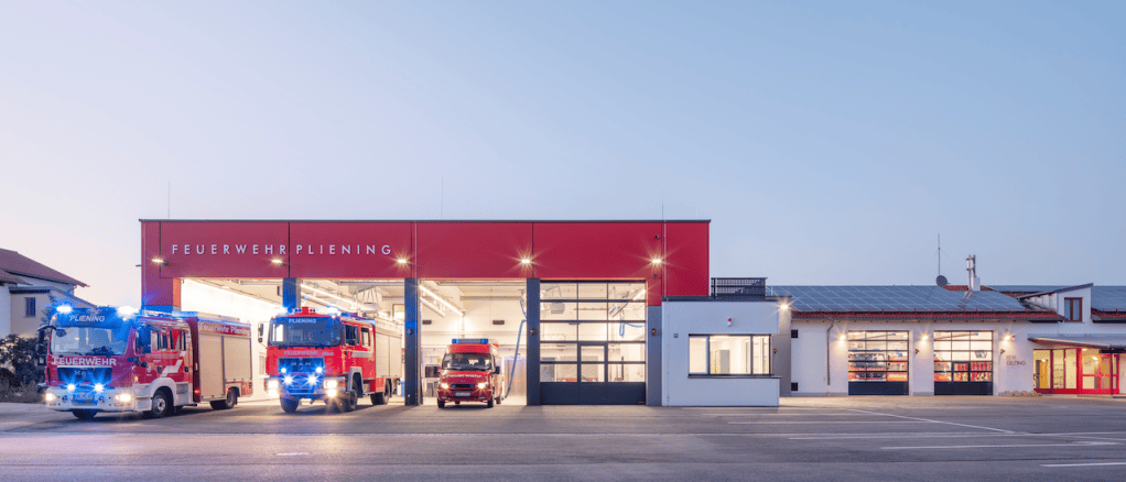 Feuerwehrhaus Pliening in der Abenddämmerung mit Einsatzfahrzeugen