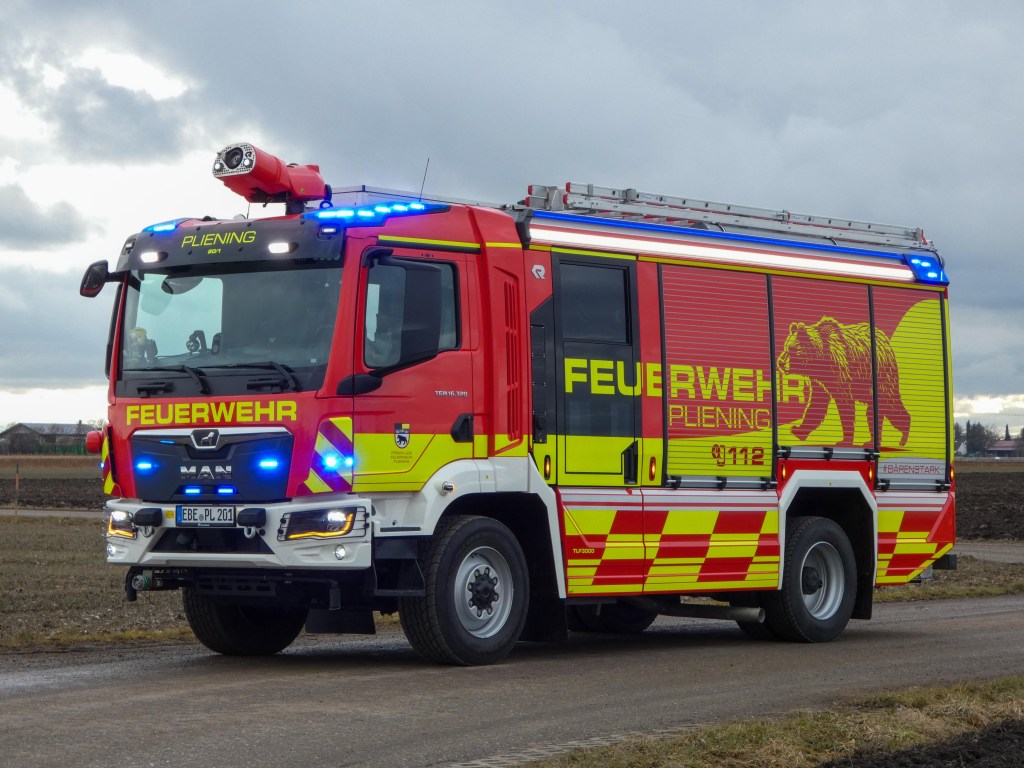 Das neue rote Löschfahrzeug der Feuerwehr Pliening mit Blaulicht, Bären-Motiv und rot-gelber Warnmarkierung auf einem Feldweg